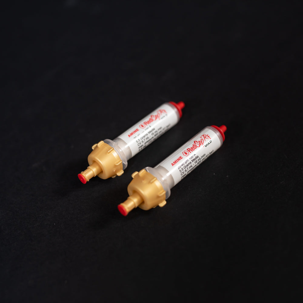 A pair of small white tubes with gold and red caps displayed on a black background, creating a striking visual contrast between the two elements.