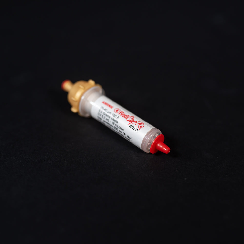 A small white tube with gold and red caps displayed on a black background, creating a striking visual contrast between the two elements.