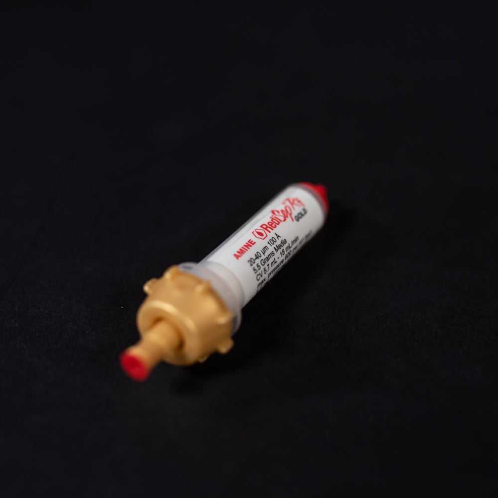 A small white tube with gold and red caps displayed on a black background, creating a striking visual contrast between the two elements.