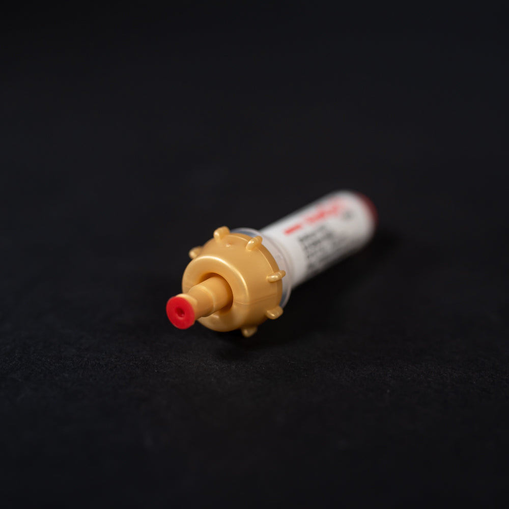 A small white tube with gold and red caps displayed on a black background, creating a striking visual contrast between the two elements.