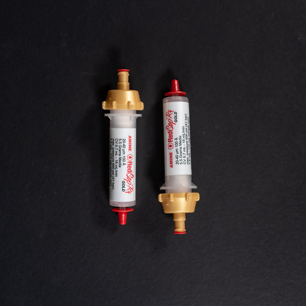 A pair of small white tubes with gold and red caps displayed on a black background, creating a striking visual contrast between the two elements.