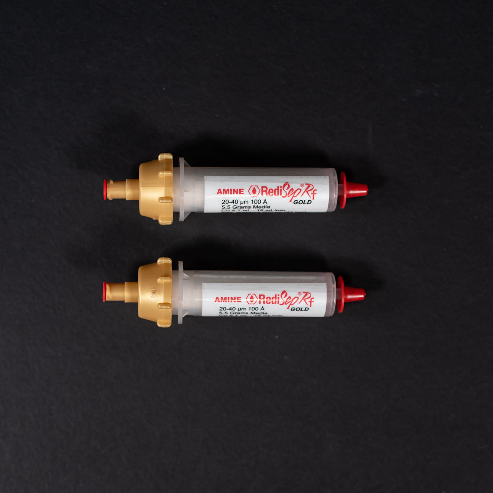 A pair of small white tubes with gold and red caps displayed on a black background, creating a striking visual contrast between the two elements.