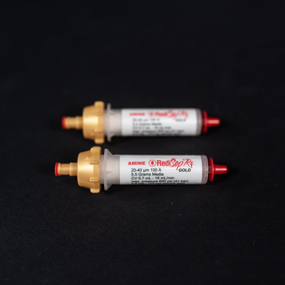 A pair of small white tubes with gold and red caps displayed on a black background, creating a striking visual contrast between the two elements.