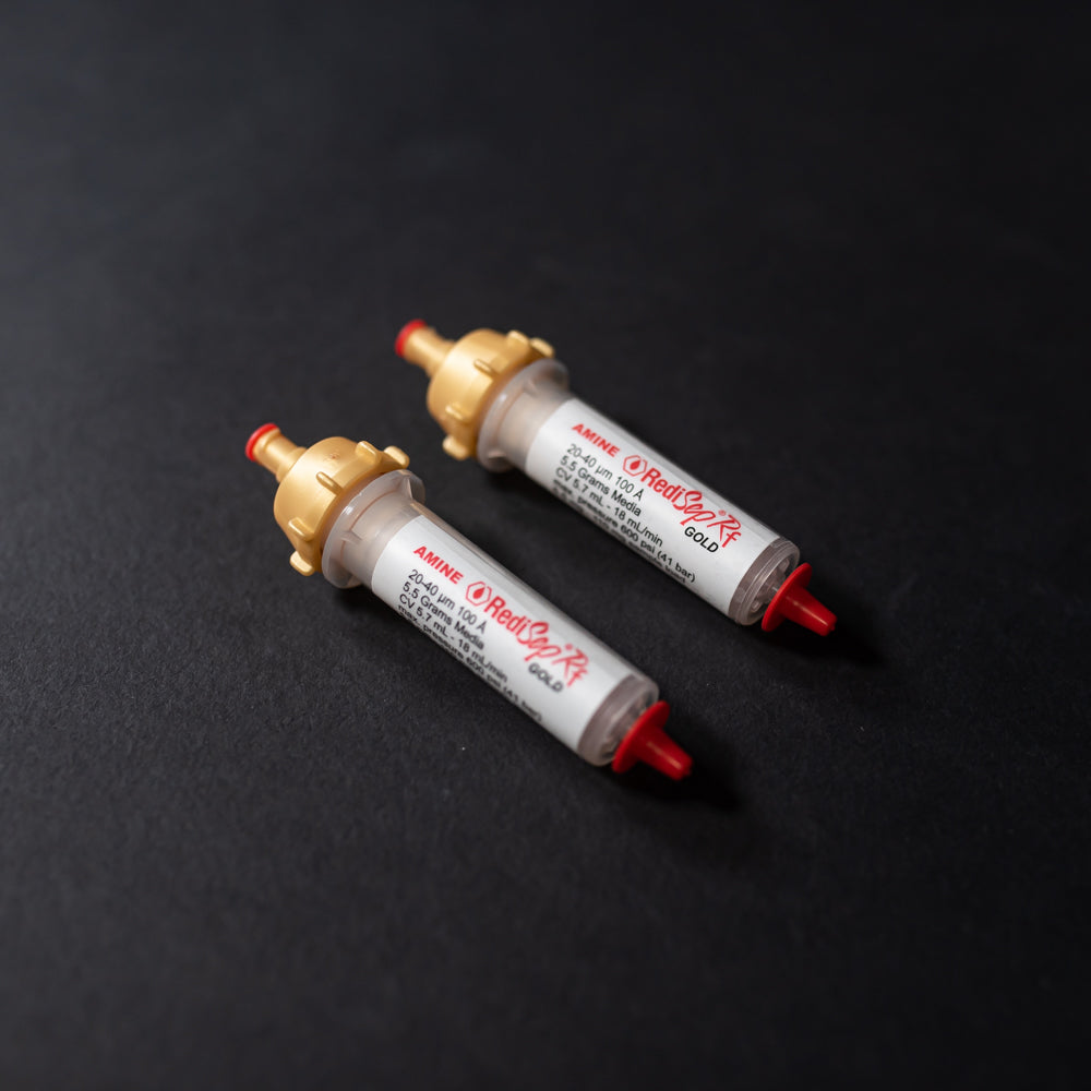 A pair of small white tubes with gold and red caps displayed on a black background, creating a striking visual contrast between the two elements.