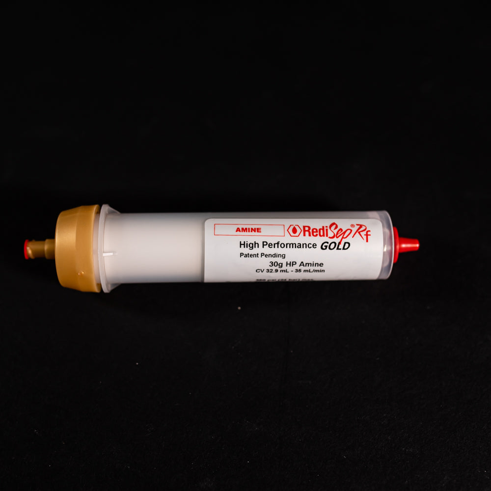 A small white tube with gold and red caps displayed on a black background, creating a striking visual contrast between the two elements.