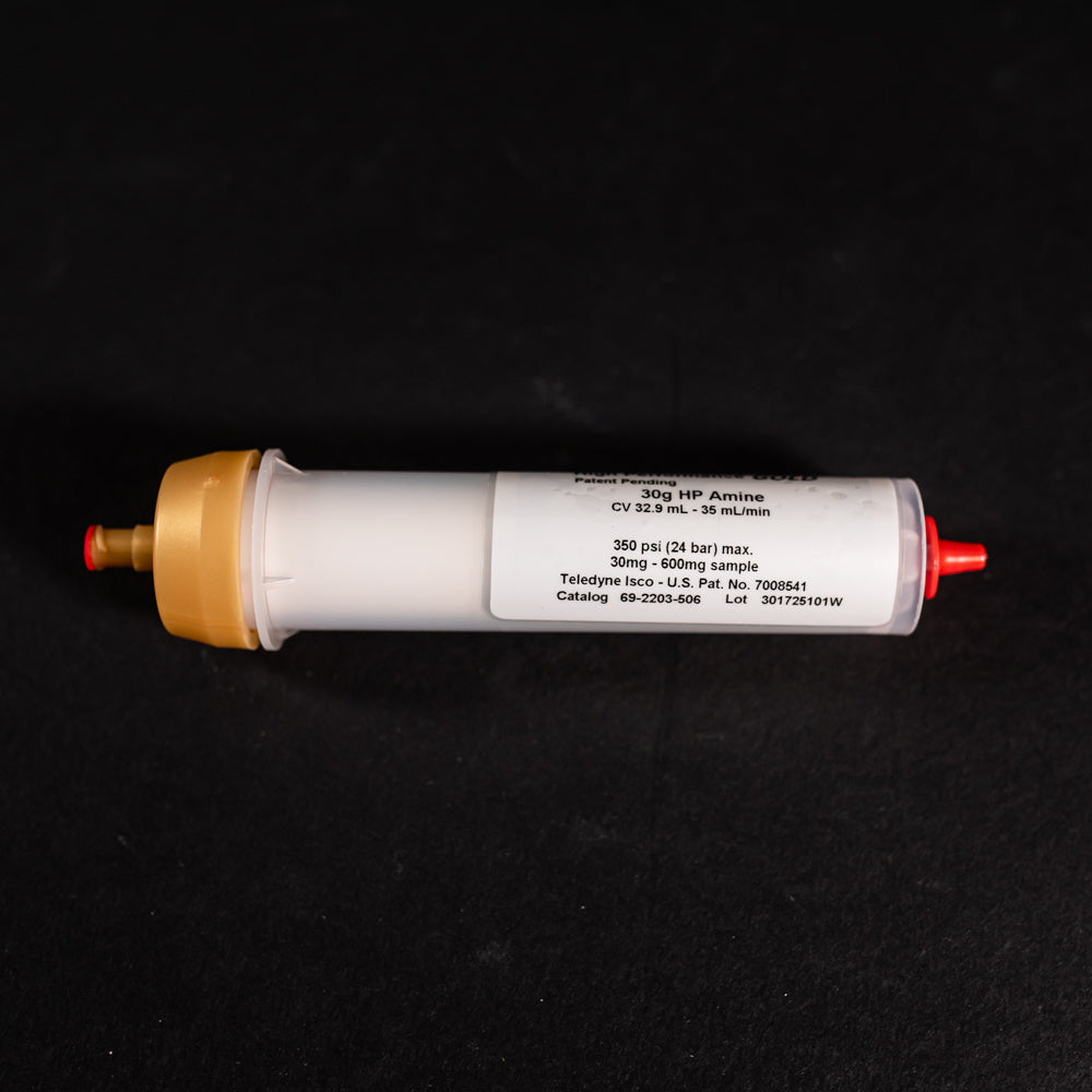 A small white tube with gold and red caps displayed on a black background, creating a striking visual contrast between the two elements.