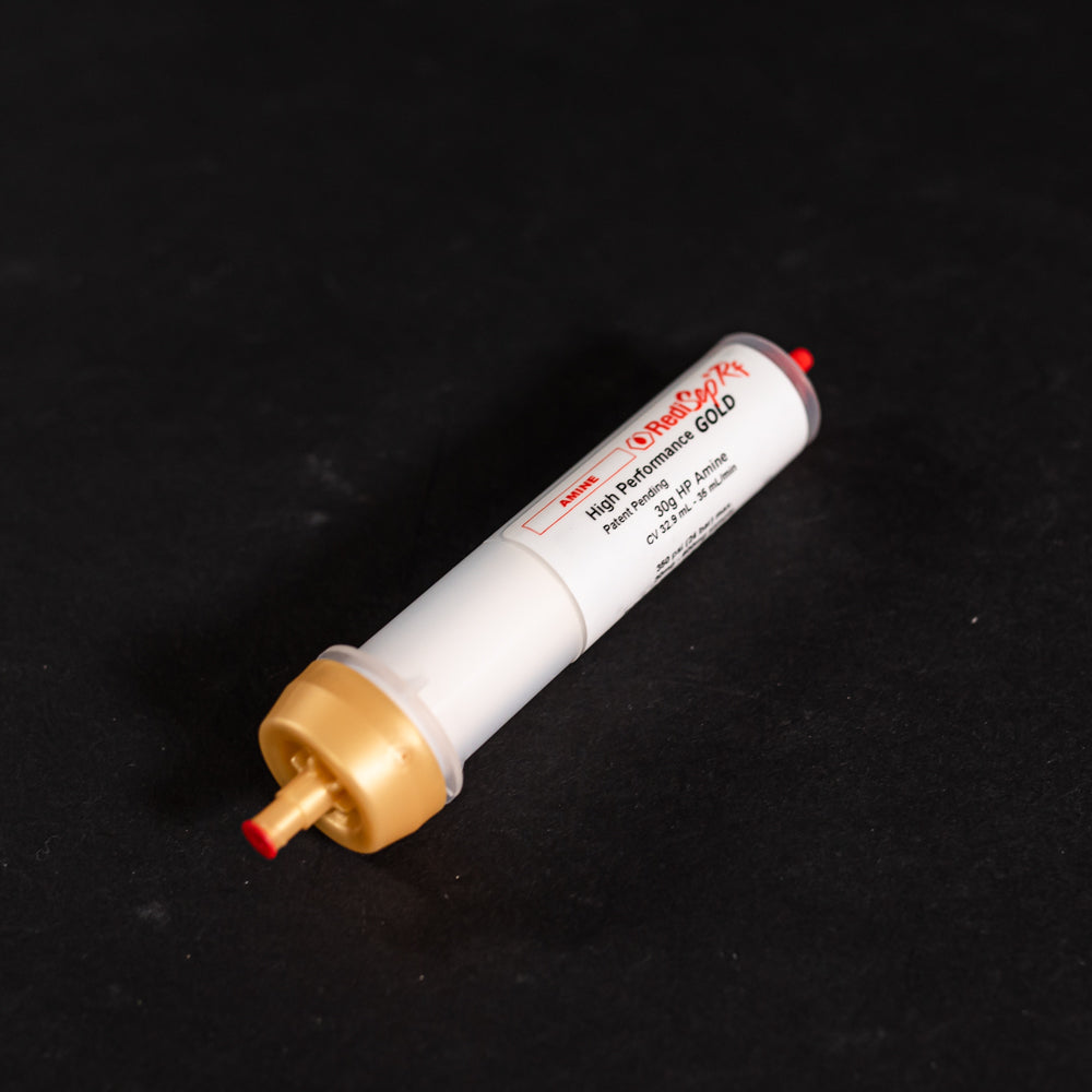 A small white tube with gold and red caps displayed on a black background, creating a striking visual contrast between the two elements.