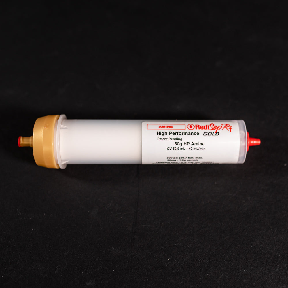 A small white tube with gold and red caps displayed on a black background, creating a striking visual contrast between the two elements.