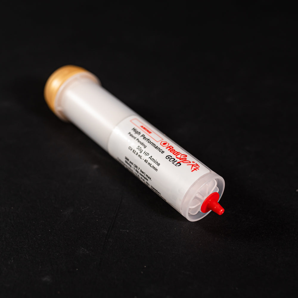 A small white tube with gold and red caps displayed on a black background, creating a striking visual contrast between the two elements.
