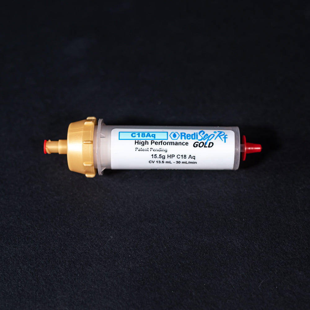 A small white tube with gold and red caps displayed on a black background, creating a striking visual contrast between the two elements.