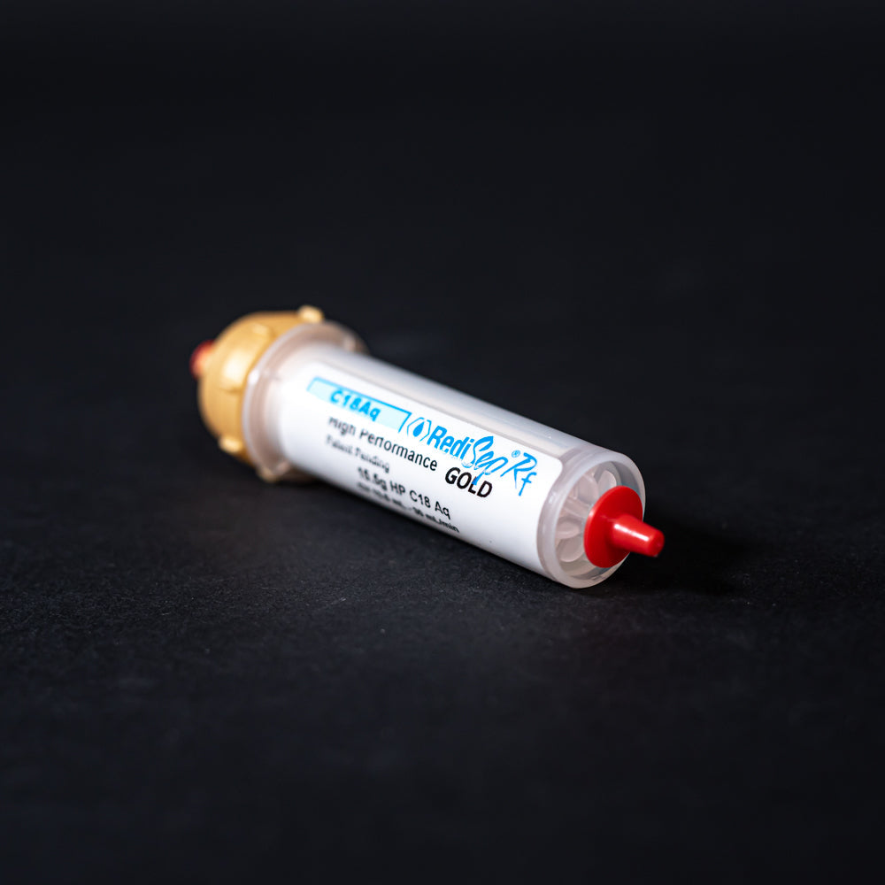 A small white tube with gold and red caps displayed on a black background, creating a striking visual contrast between the two elements.