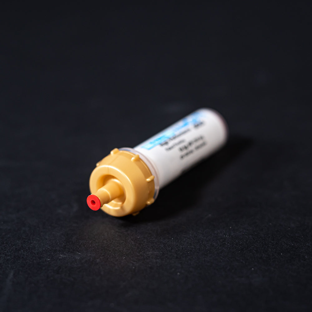 A small white tube with gold and red caps displayed on a black background, creating a striking visual contrast between the two elements.