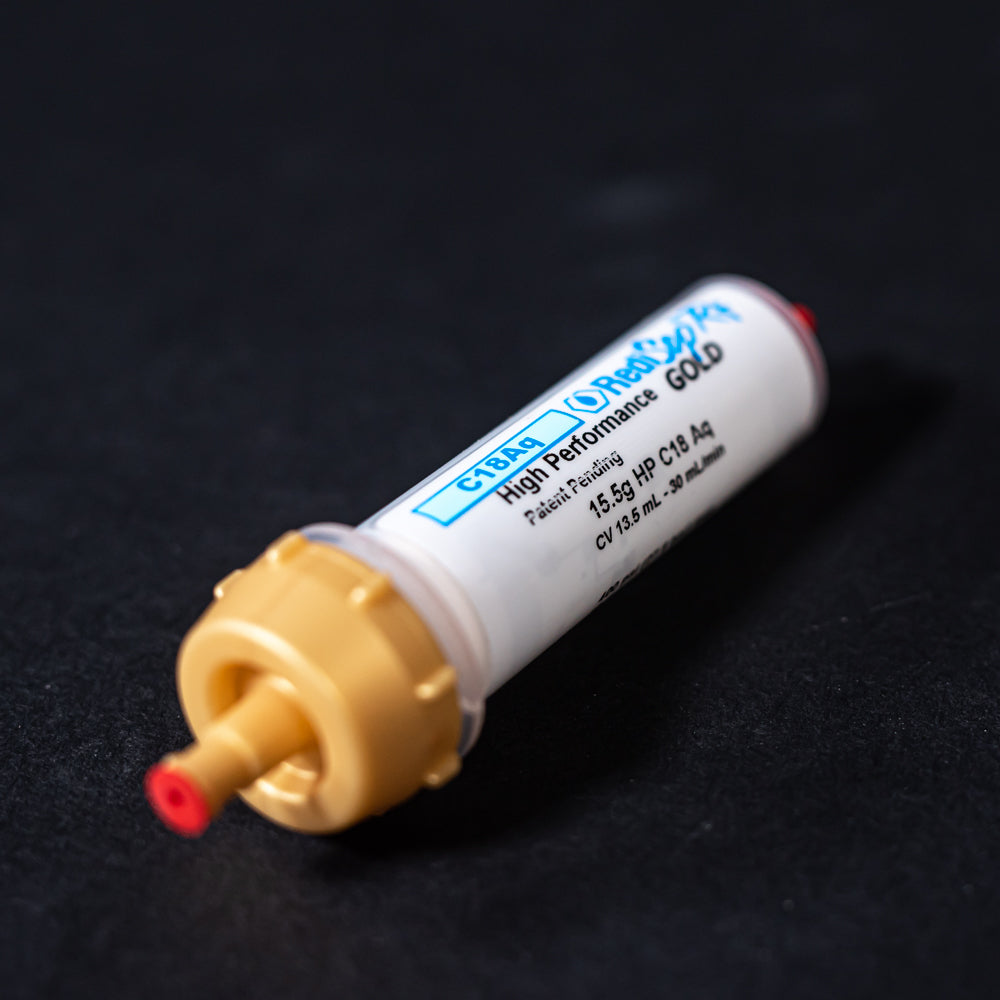 A small white tube with gold and red caps displayed on a black background, creating a striking visual contrast between the two elements.