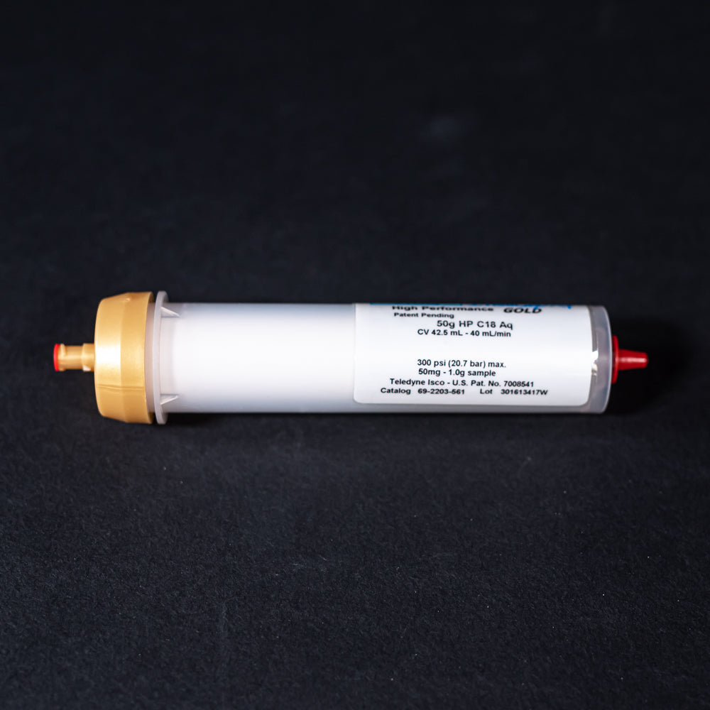 A small white tube with gold and red caps displayed on a black background, creating a striking visual contrast between the two elements.