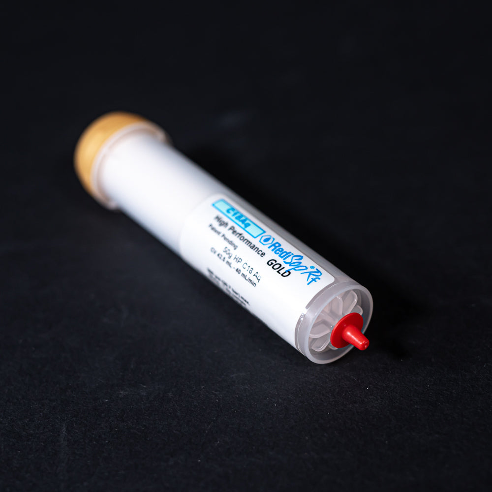 A small white tube with gold and red caps displayed on a black background, creating a striking visual contrast between the two elements.