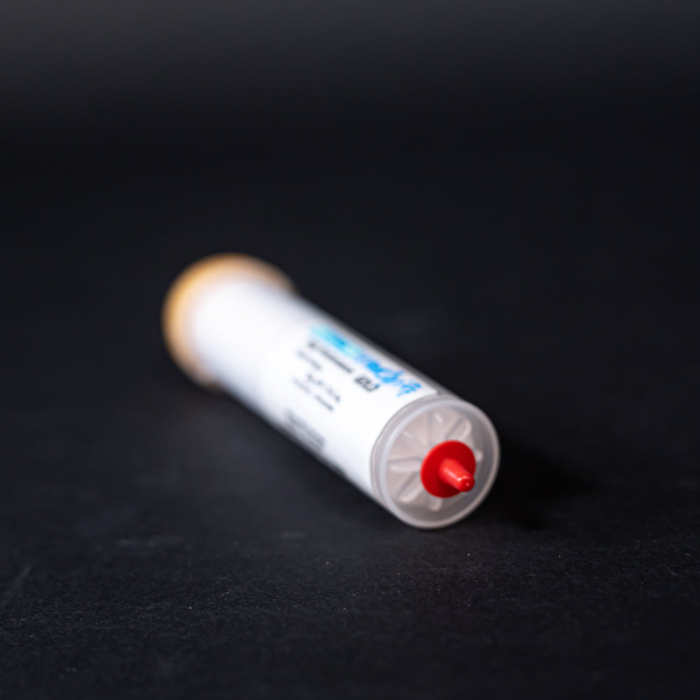 A small white tube with gold and red caps displayed on a black background, creating a striking visual contrast between the two elements.
