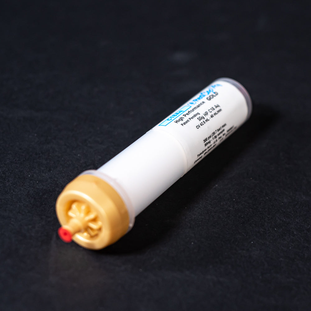 A small white tube with gold and red caps displayed on a black background, creating a striking visual contrast between the two elements.