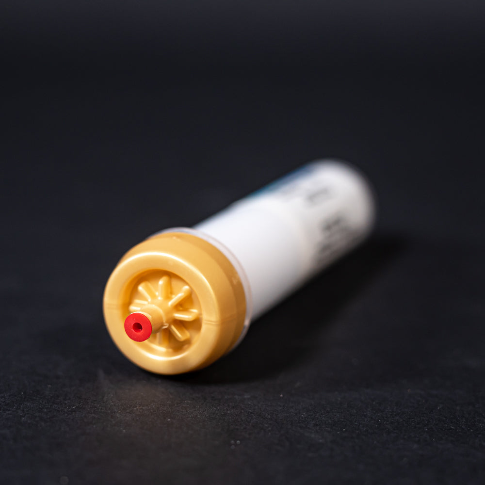 A small white tube with gold and red caps displayed on a black background, creating a striking visual contrast between the two elements.