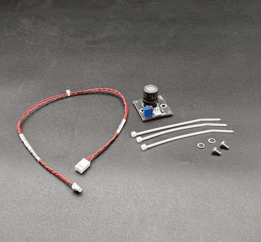 A small electronic component kit on a dark gray textured background, including a red and white wire with white connectors, a small circuit board with a black cylindrical component, four white zip ties, and two small screws.